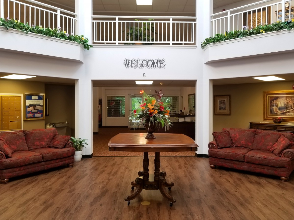 A welcoming lobby area featuring a central table with floral arrangement, surrounded by comfortable sofas and decorative plants.