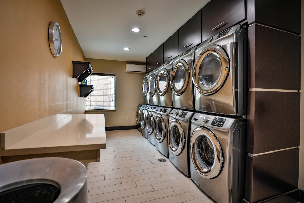 A modern laundry room featuring multiple washing machines and dryers lined up against the wall.