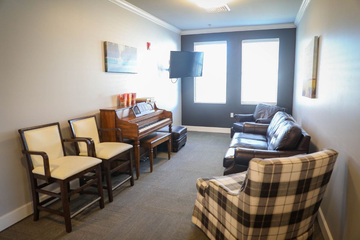 A cozy living room with a piano, comfortable seating, and a television mounted on the wall.