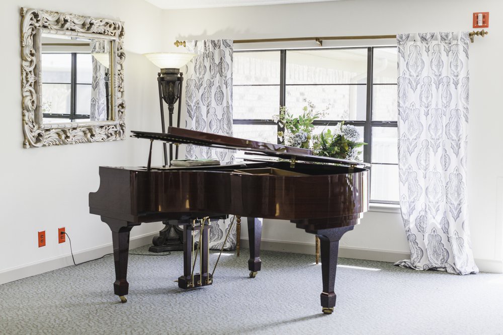 A grand piano elegantly positioned in a well-lit room with large windows and decorative curtains.