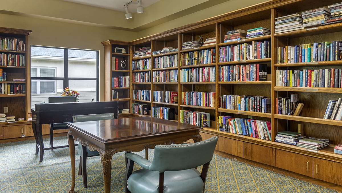 A cozy library room with bookshelves filled with books, a wooden table, and two chairs.