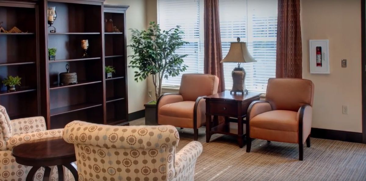 A cozy living room with two armchairs, a side table holding a lamp, and a bookshelf in the corner.