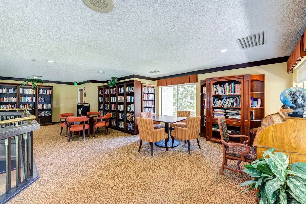 A cozy library room with bookshelves, tables, and chairs arranged for reading.
