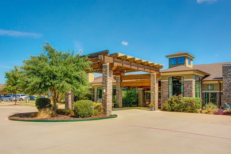 A sunny day view of a building entrance with a landscaped driveway.