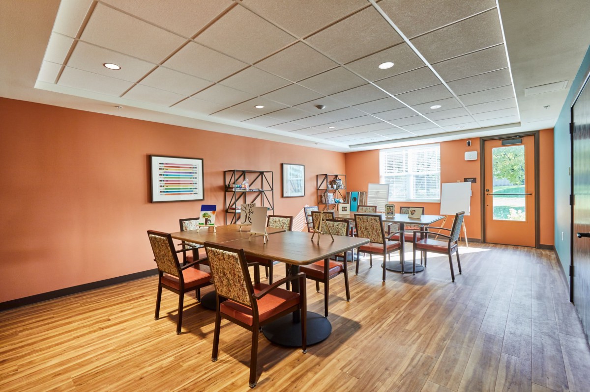 A spacious meeting room with tables and chairs, featuring wooden flooring and art on the walls.