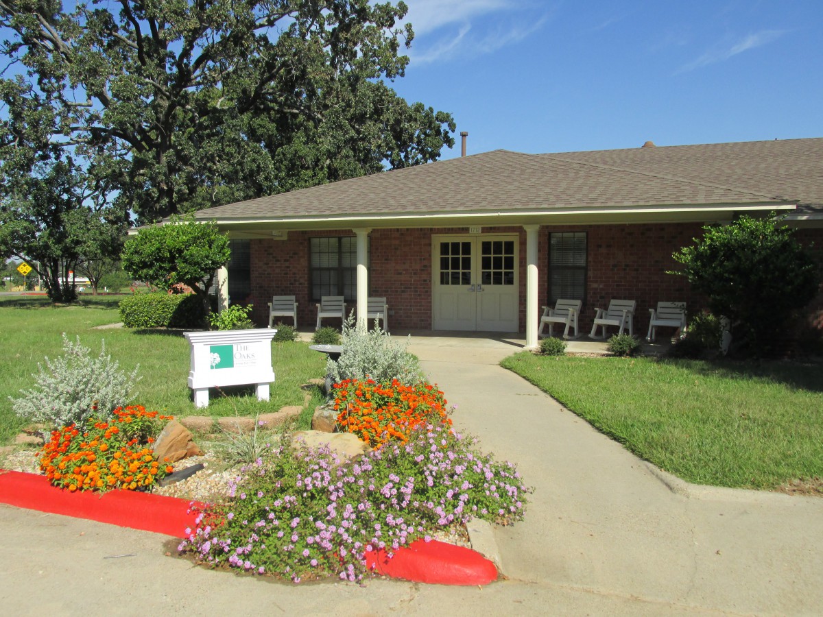 A charming brick building with a landscaped garden and outdoor seating on a sunny day.