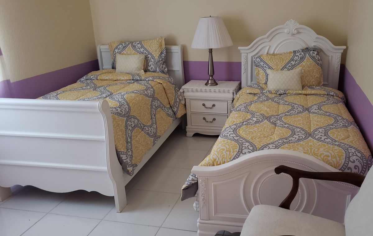 A cozy bedroom featuring two twin beds with matching yellow and gray bedding, separated by a white nightstand with a lamp.