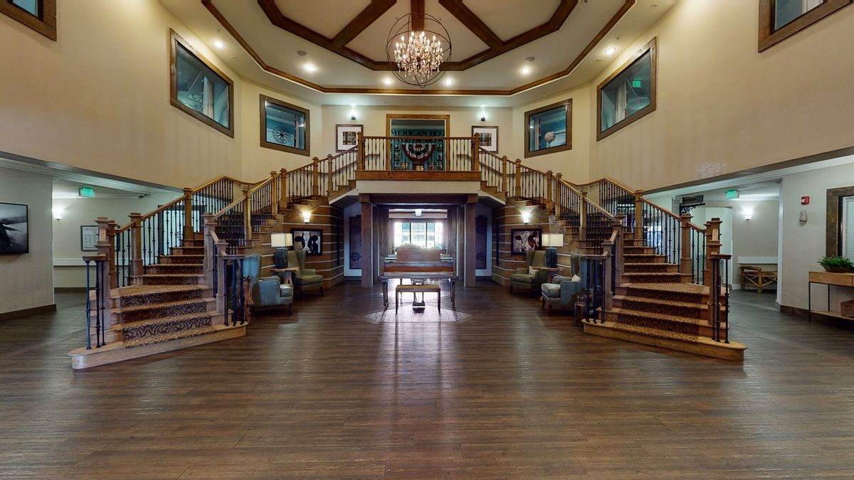 A grand interior lobby with a central chandelier, symmetrical staircases, and wood flooring.