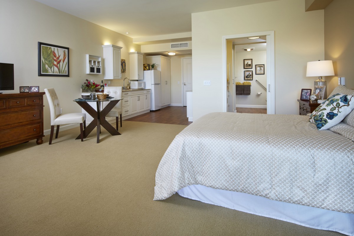 A cozy studio apartment featuring a bedroom area, desk, and kitchenette.