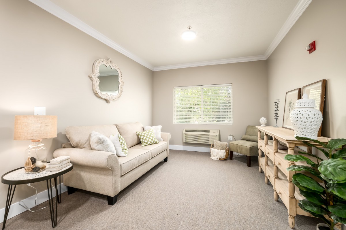 A cozy living room with beige tones, featuring a sofa, armchair, and decorative mirror.
