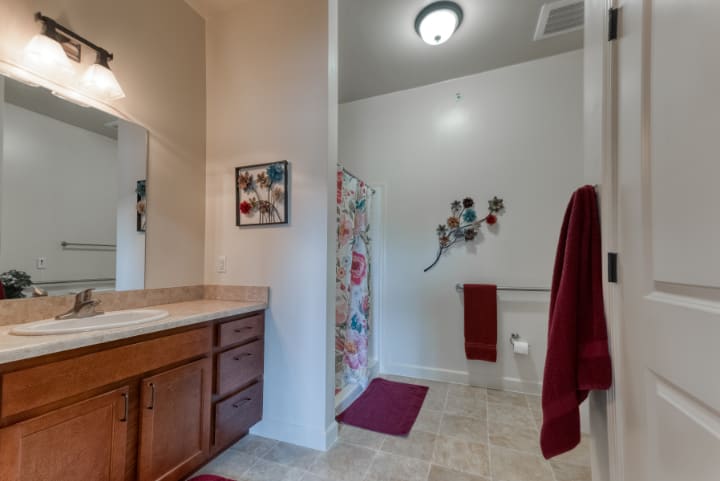 A well-lit bathroom with a sink, mirror, and a shower area decorated with red towels and floral accents.