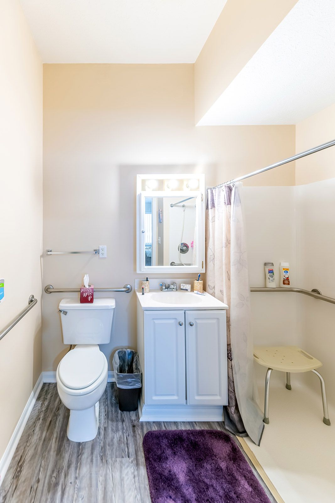 A clean and bright bathroom featuring a sink, toilet, shower with curtain, and a mirror above the white cabinet.