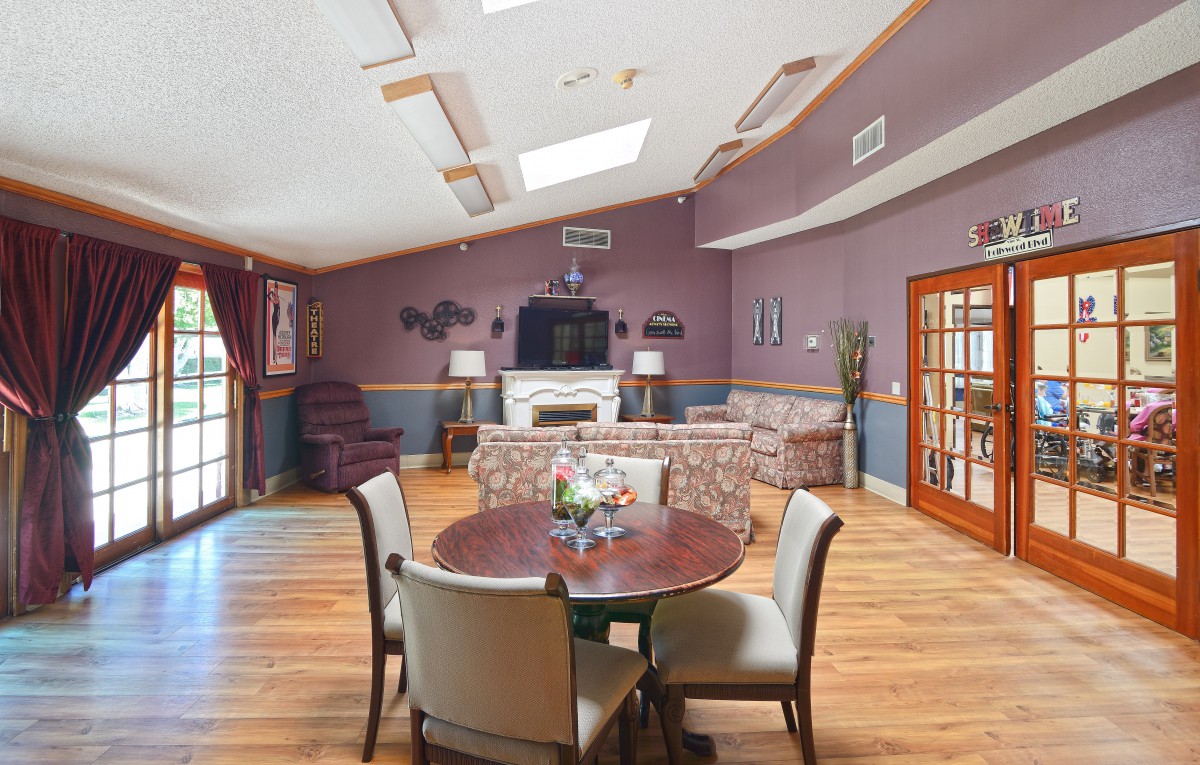 A spacious living room with modern furniture, featuring a seating area around a fireplace and a round table with chairs.