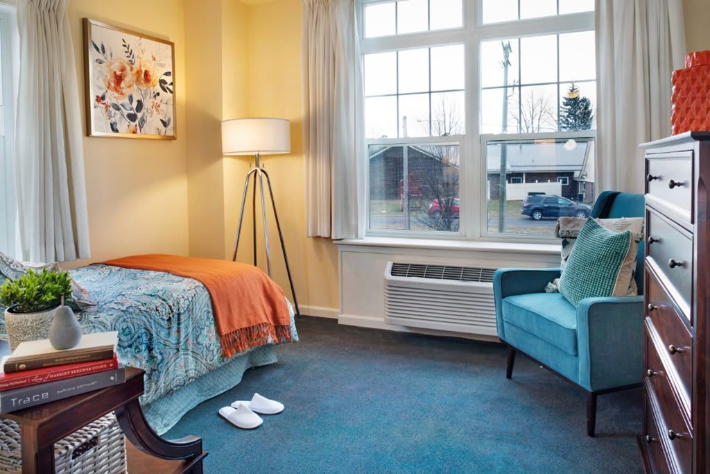 A cozy bedroom with a single bed, blue chair, and large window.