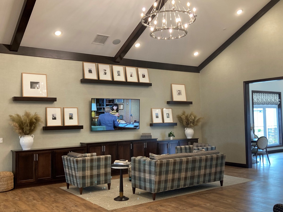 A stylish living room with a modern chandelier, patterned sofas, a mounted television, and decorative artwork on shelves.