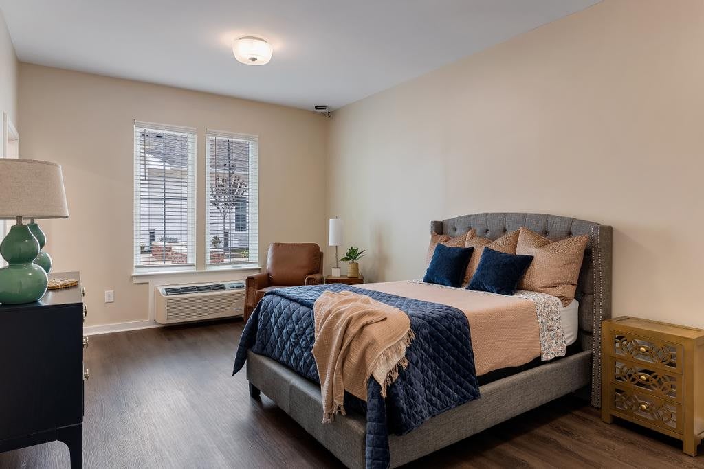 A modern bedroom with a stylish bed and cozy decor, featuring large windows and hardwood flooring.