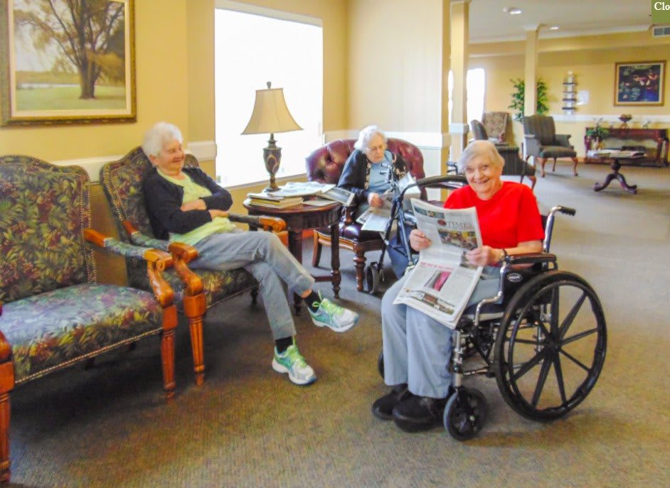 A group of seniors relaxing in a cozy common area, with one reading a newspaper.