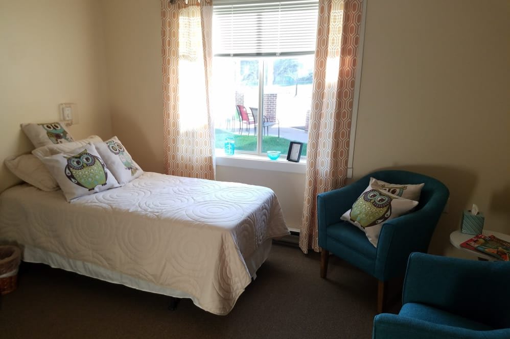 A cozy bedroom with a bed, chair, and large window letting in natural light.