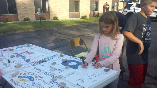 A young girl is engaged in signing or drawing on a large table at an outdoor event.