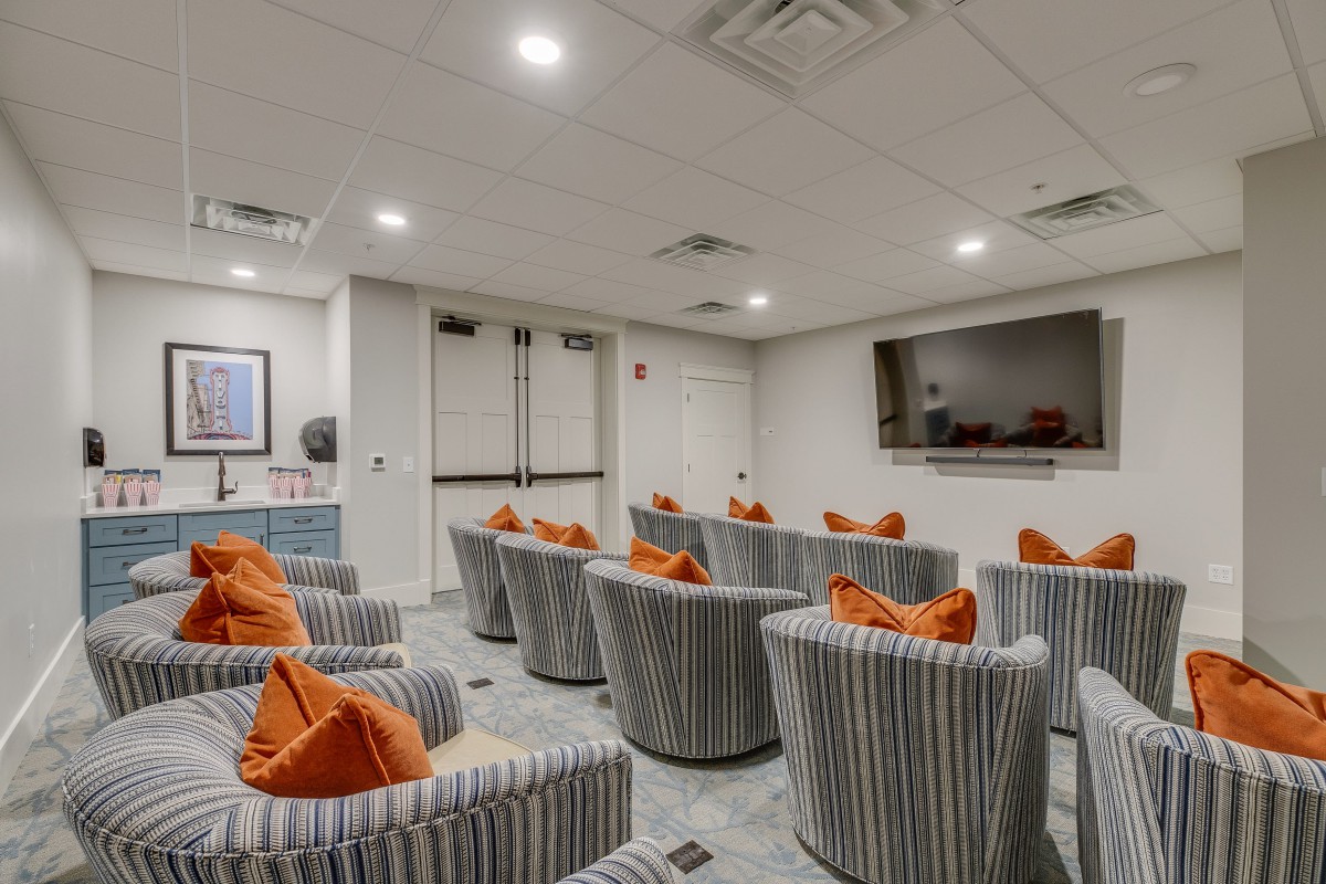 A cozy home theater with striped seating and orange pillows facing a large screen.