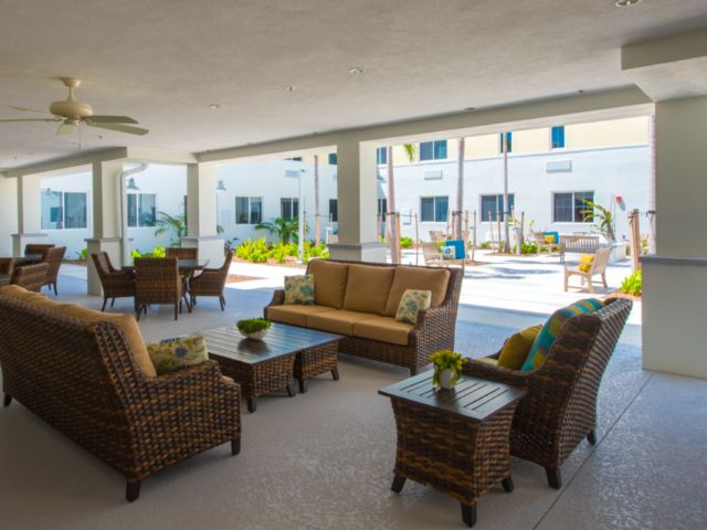 A well-furnished outdoor seating area with wicker chairs and a sofa set under a covered patio in an apartment complex.