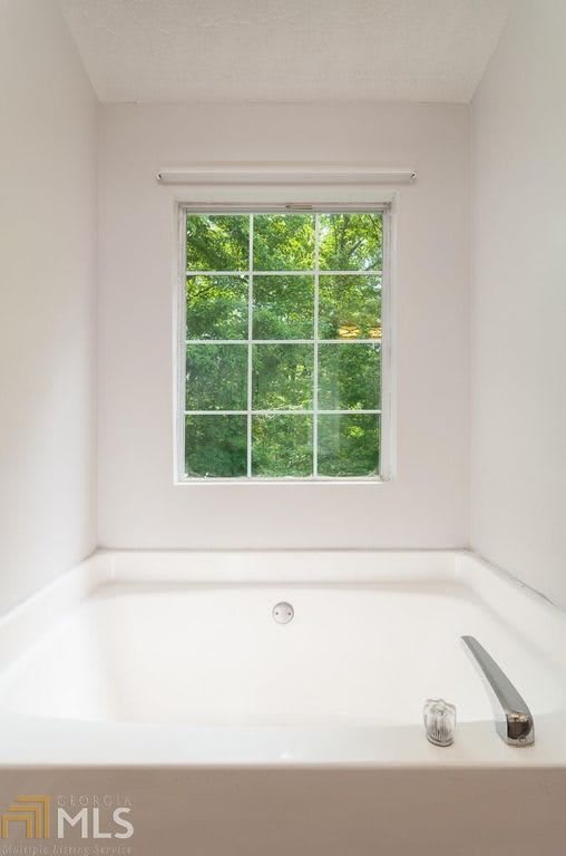 A white bathtub situated beneath a window with a view of greenery outside.