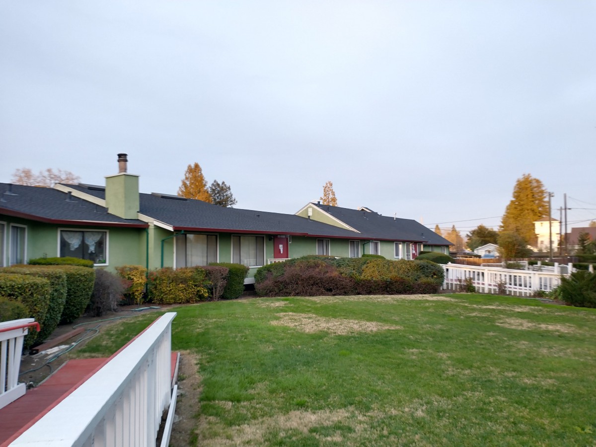 A suburban house with a well-maintained lawn and surrounding fence, set against an autumn backdrop.