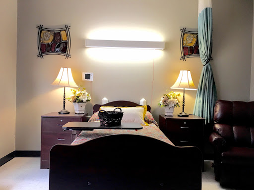 A well-lit hospital room featuring a bed, nightstands with lamps, and artwork on the walls.
