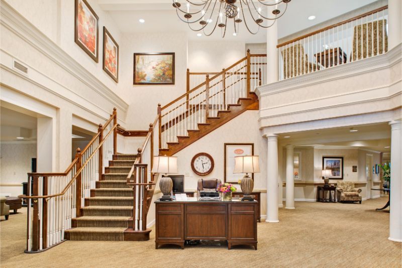 A spacious office reception area featuring a grand staircase, a chandelier, and elegant furnishings.