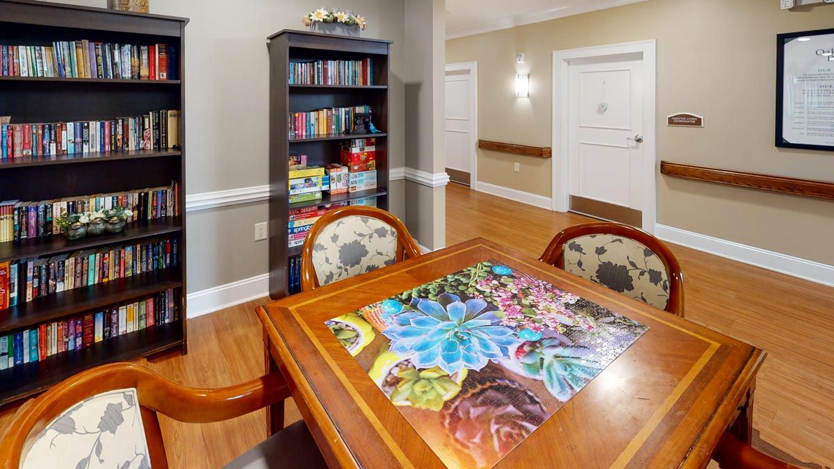 A cozy room featuring a completed puzzle on a wooden table with surrounding chairs and a bookshelf filled with books.