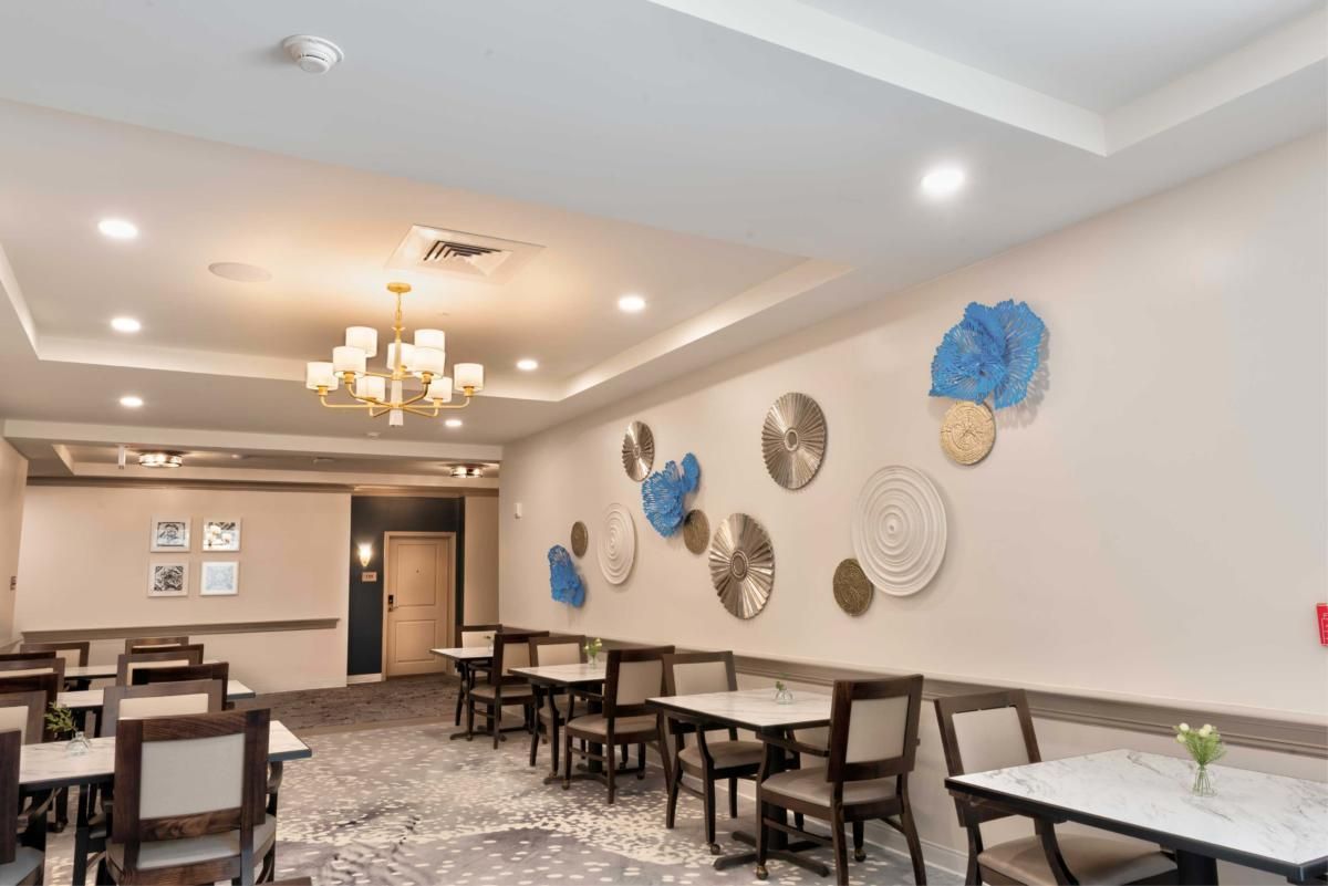 A modern restaurant interior featuring elegant chandeliers, contemporary artwork, and neatly arranged tables and chairs.