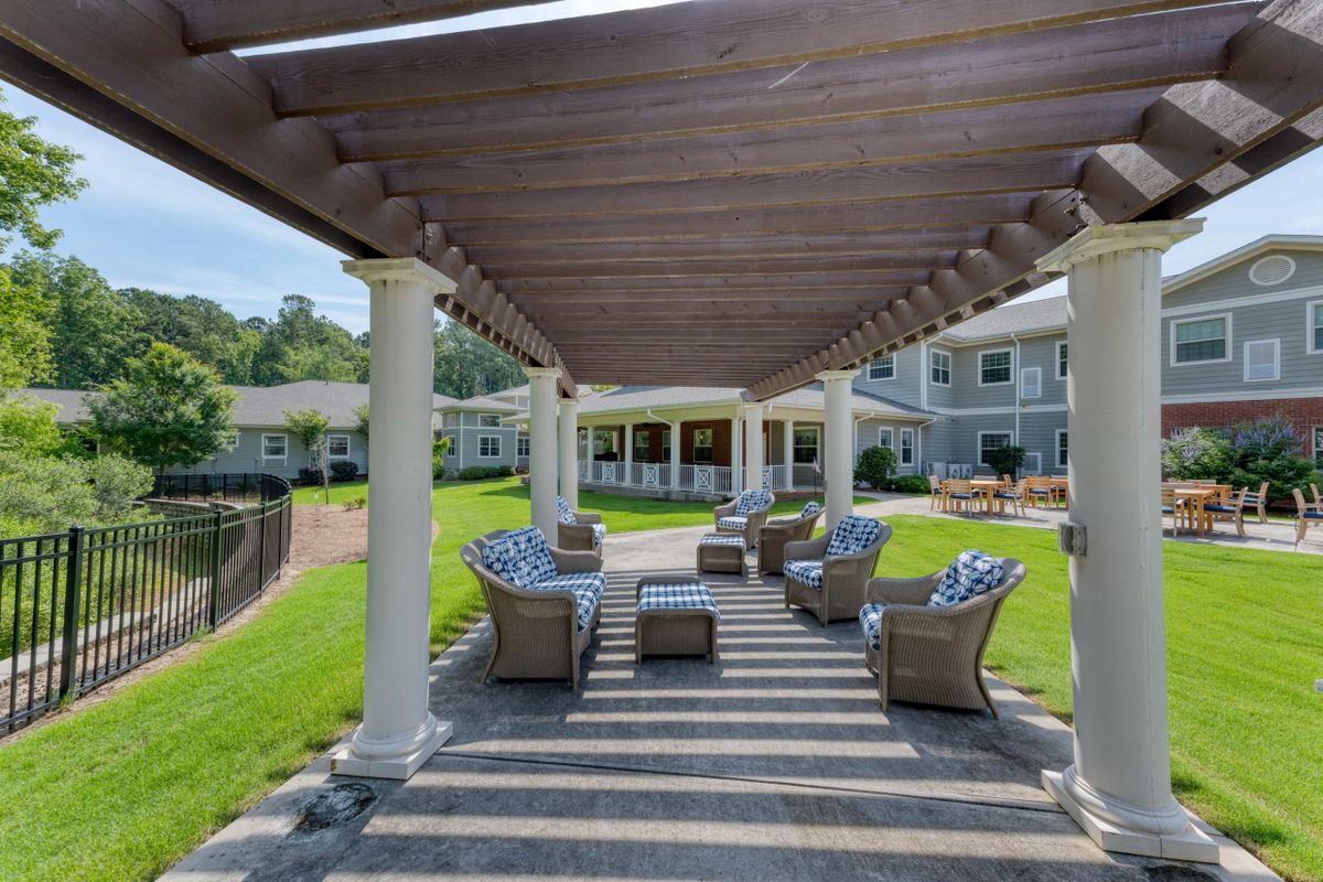 A tranquil outdoor seating area under a pergola with patio furniture in a sunny garden.
