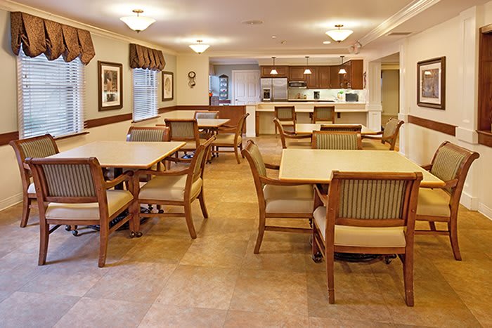 A cozy dining room with multiple tables and chairs, adjacent to a kitchen area.
