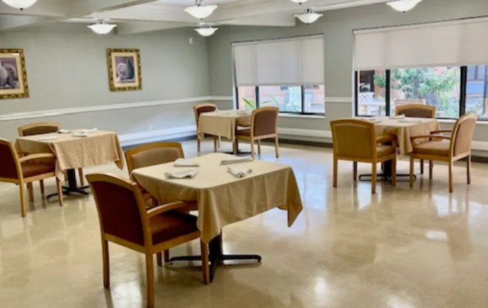 An empty dining room with neatly arranged tables and chairs, featuring soft indoor lighting and large windows.