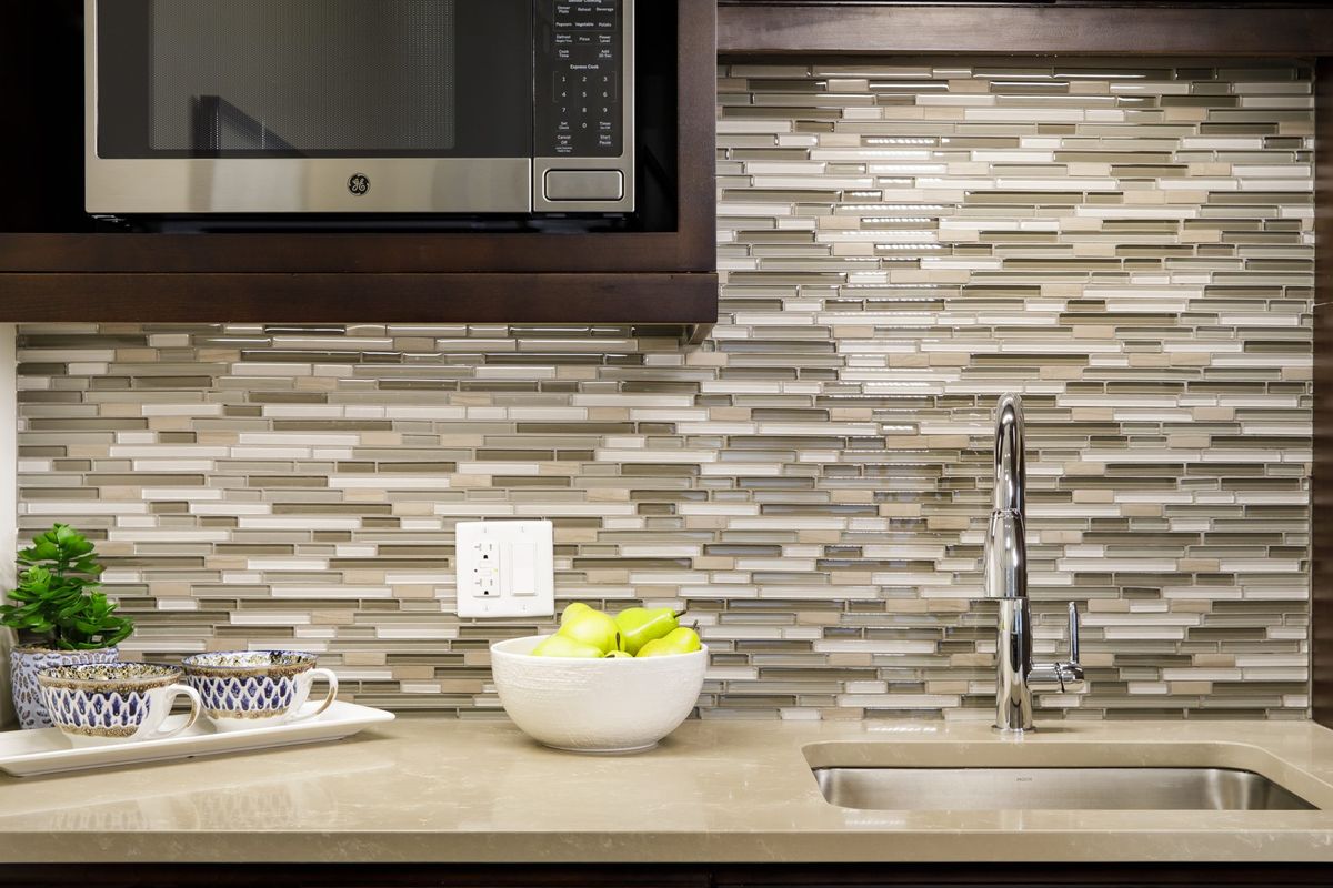 Modern kitchen with a tile backsplash, featuring a microwave, sink, and fruit bowl on the countertop.