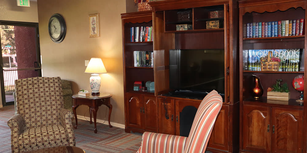 A cozy living room with a wooden bookshelf, television, and striped armchair.