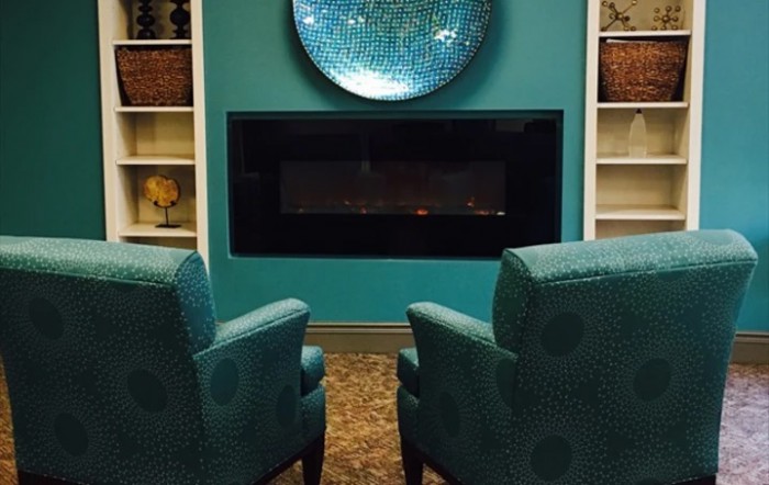 A cozy living room with turquoise armchairs facing a modern fireplace.