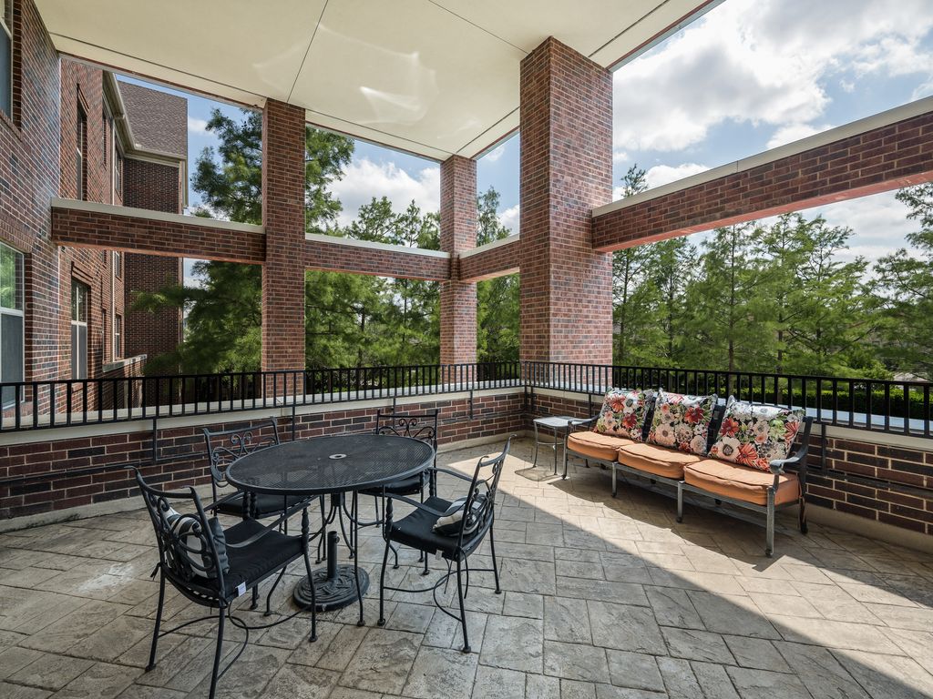 A spacious outdoor patio with a table and chairs, cushioned seating, and surrounded by a brick structure.