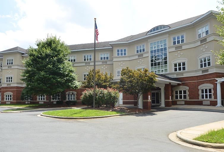 A three-story building with an American flag in front, surrounded by trees and a landscaped entrance.
