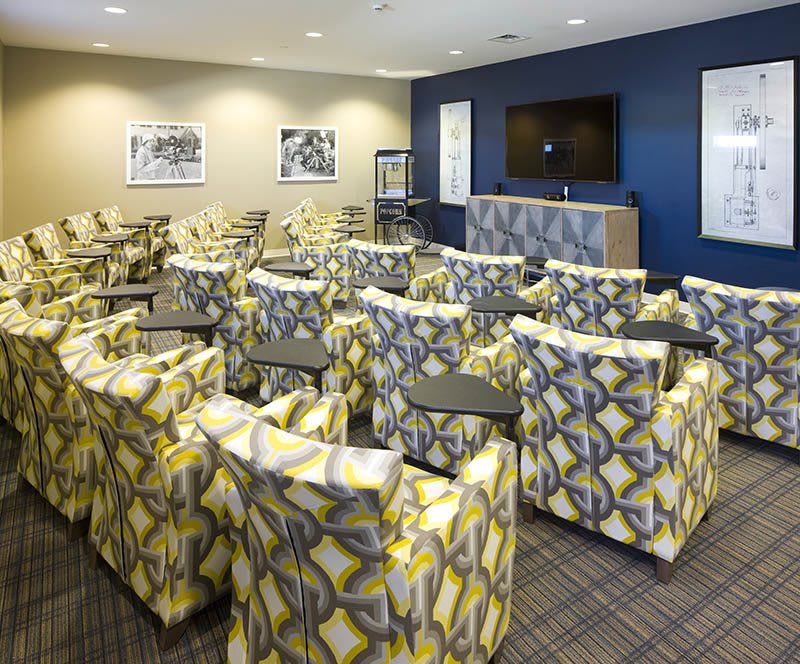 A modern conference room with patterned chairs arranged in rows facing a large screen.