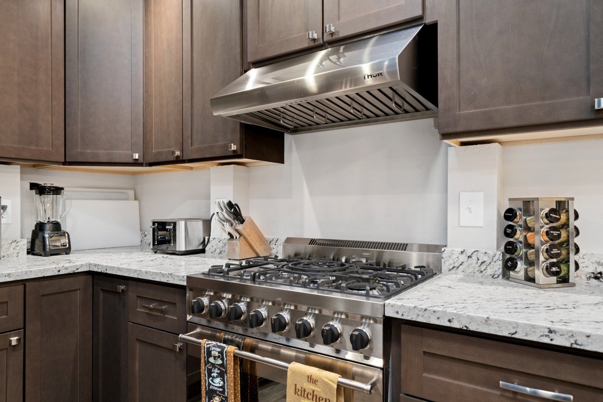 A modern kitchen featuring a stainless steel stove with a range hood and surrounding countertops.