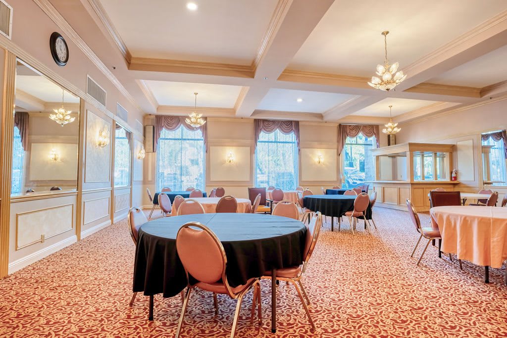 An elegant conference room with round tables and chairs, featuring chandeliers and large windows.