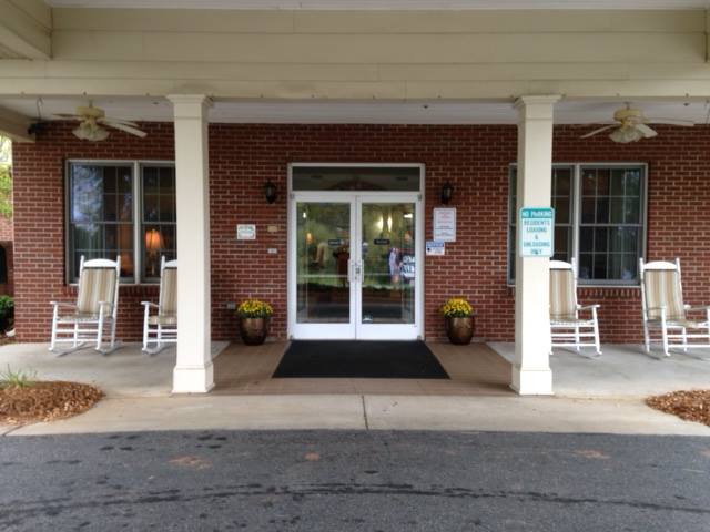 Front entrance of a building with double glass doors and rocking chairs on the porch.