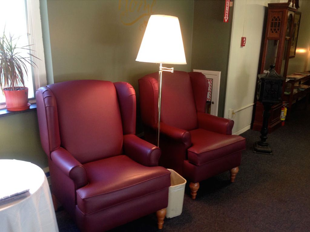 Two red armchairs with a lamp in between them, placed against a green wall.