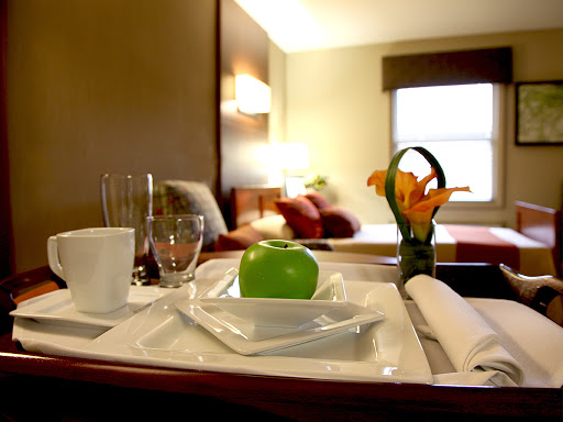 A neatly arranged room service breakfast tray featuring a green apple and floral decoration in a hotel room.