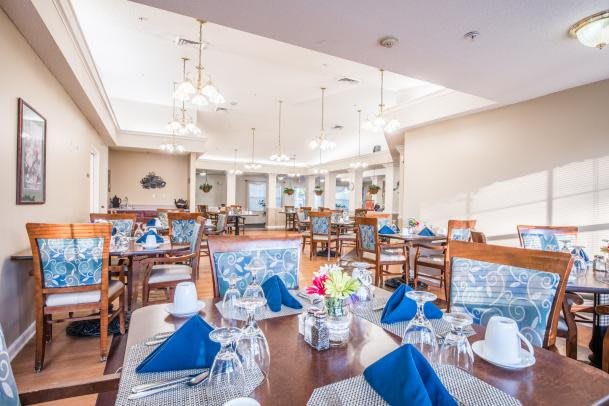 An elegantly set dining room with tables prepared for guests, featuring blue napkins and decorative centerpieces.