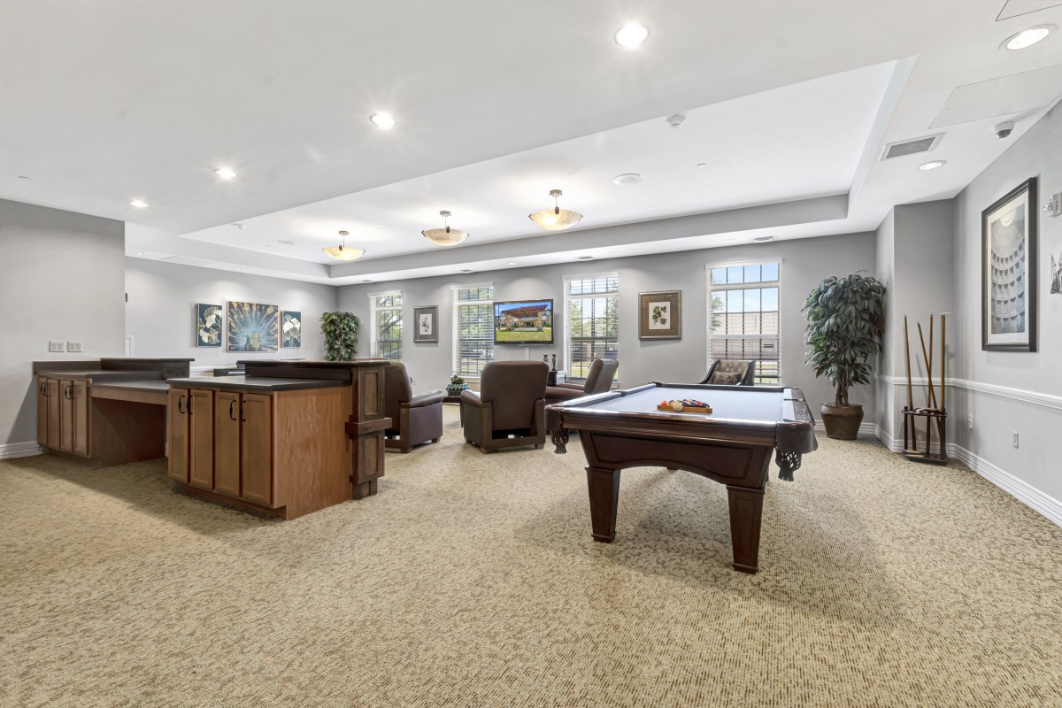 A spacious game room featuring a billiard table, comfortable seating, and decorative artwork on the walls.