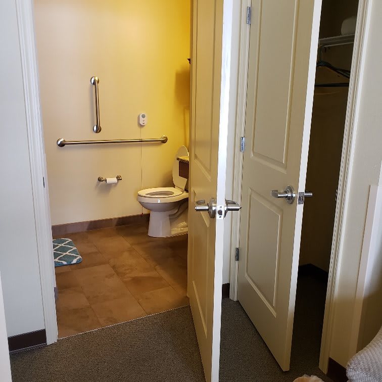 Open door view of a bathroom with a toilet and handrail.