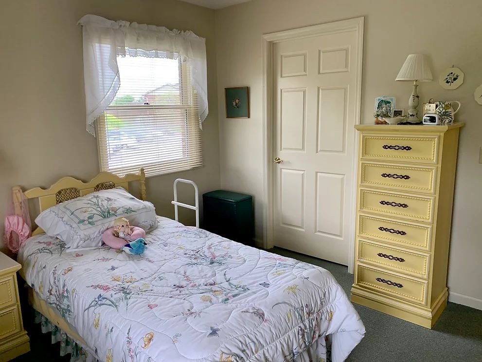A cozy bedroom with a single bed, a dresser, and light streaming through the window.