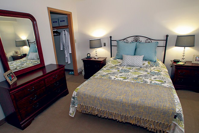 A cozy bedroom with a neatly made bed, bedside lamps, and an open closet.